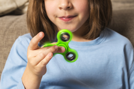 little girl playing with green fidget spinner toy to relieve stress at home