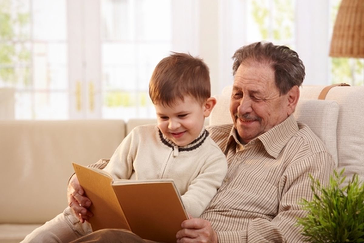 Happy grandfather sitting in armchair and reading book to his grandson, smiling.