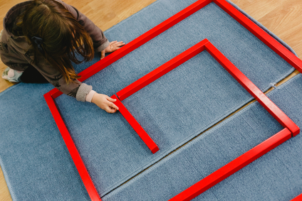 Girl is a class of a school placing the red bars montessori on a mat.