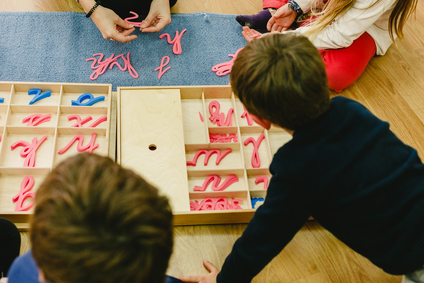Group of elementary students learning grammar with montessori materials within their classroom in a collegiate of alternative pedagogy.
