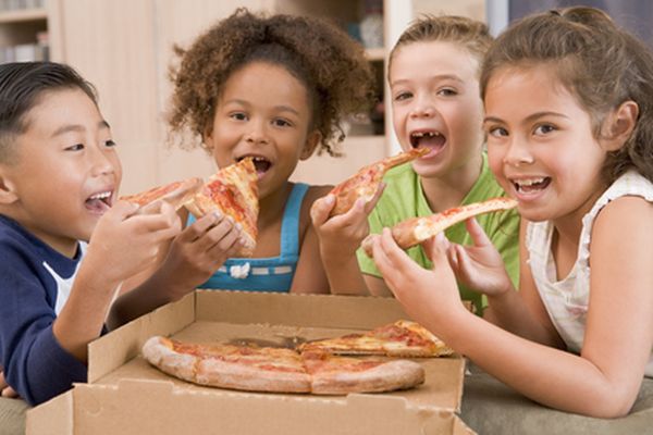 Four young children indoors eating pizza smiling